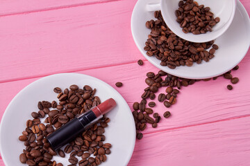 Top view plates with coffee beans and lipstick. Pink wooden desk.