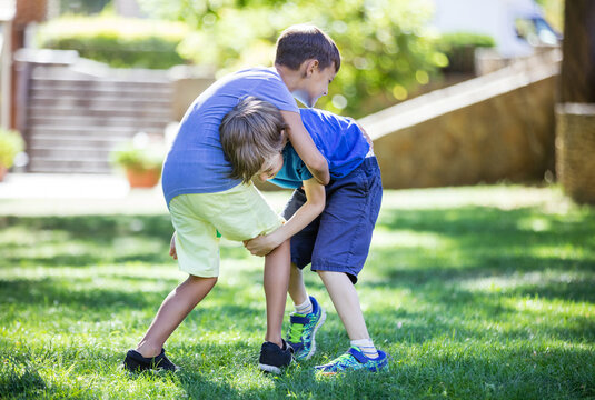 Two boys fighting outdoors. Siblings or friends wrestling on grass in summer park