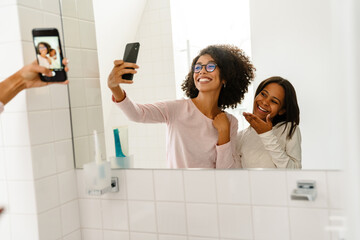 Black girl and her mother taking selfie on cellphone in bathroom