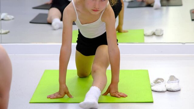 The child trains in the dance studio in the hall on the mat, does stretching exercises and abs, sits on the splits. Working on yourself and your body since childhood, overcoming yourself