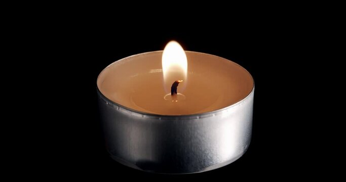 A single small candle burning.Isolated candle burning with dark background. Little paraffin candle with yellow shades burns on a black background. Background or illustration