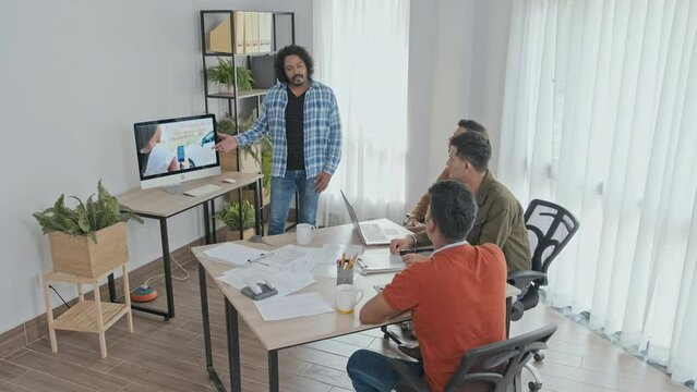 Medium slowmo of enthusiastic Indian man making presentation to his colleagues, discussing marketing and statistics in office