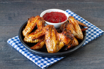 Grilled spicy chicken wings with ketchup on a plate on a table.