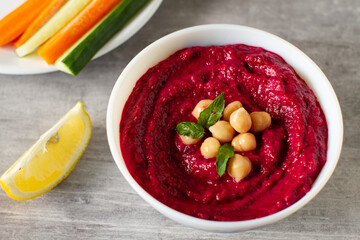 Roasted beet hummus with vegetables in a ceramic bowl on a gray background. 