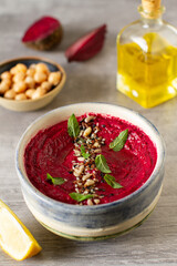 Roasted beet hummus with vegetables in a ceramic bowl on a gray background. 