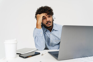 Adult indian tired curly man sitting in front of laptop