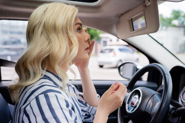 Fototapeta na wymiar Side view of blonde woman looking at mirror in car
