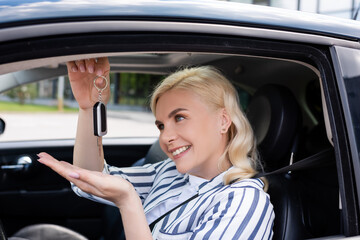 Fototapeta na wymiar Blonde driver looking at key while sitting in auto