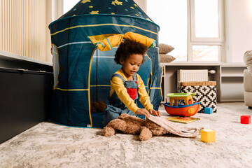 Little african american boy playing with toys sitting in tent at home © Drobot Dean