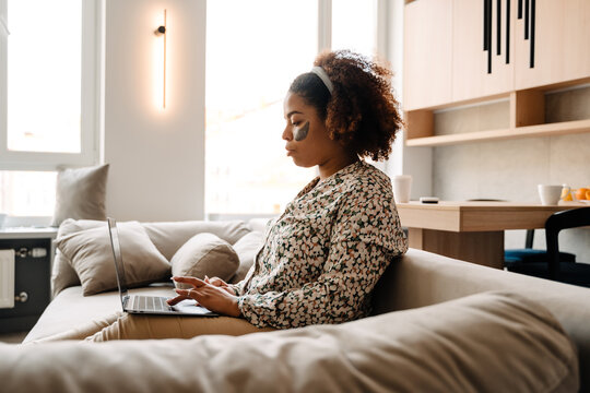 Young beautiful calm african woman working with laptop on sofa