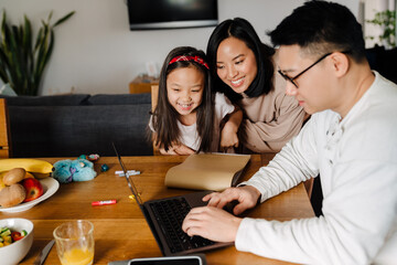 Happy asian family with daughter using laptop over table at home
