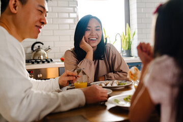 Happy asian family with little daughter having breakfast at home