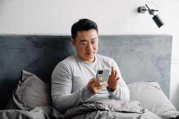 Asian man using mobile phone after sleep while sitting in bed