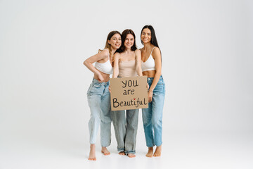 Three young attractive ladies pose and hold poster isolated