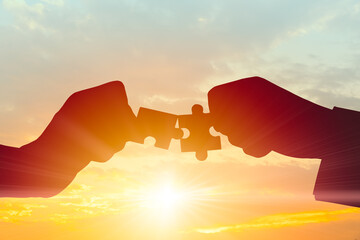 Business Teamwork, Join partnership and cooperation concept. Silhouette of two hands joining two pieces of puzzle connect together on morning sky.