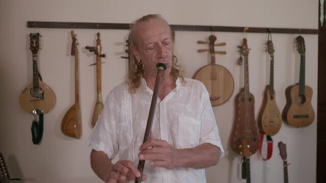 Elderly caucasian man multi-instrumentalist musician playing ney, turkish wind musical instrument in his home studio. 4K