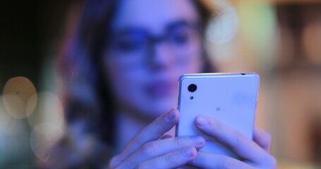 Girl wearing glasses checking cellphone at night in city atmosphere