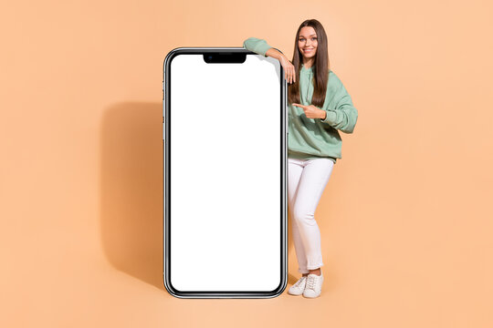 Full length body size view of beautiful trendy cheerful girl demonstrating copy space isolated over beige pastel color background