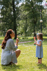 family, motherhood and people concept - happy mother with little daughter blowing soap bubbles at...