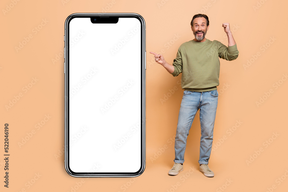 Sticker Full size photo of excited delighted man direct finger empty space raise fist isolated on beige color background