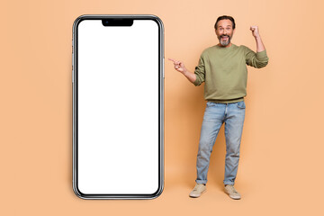 Fototapeta na wymiar Full size photo of excited delighted man direct finger empty space raise fist isolated on beige color background