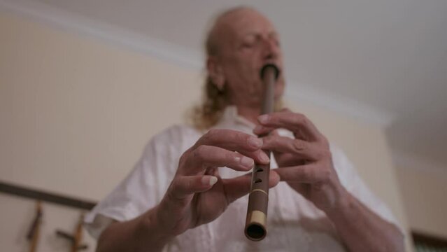 Elderly caucasian man multi-instrumentalist musician playing ney, turkish wind musical instrument in his home studio. 4K