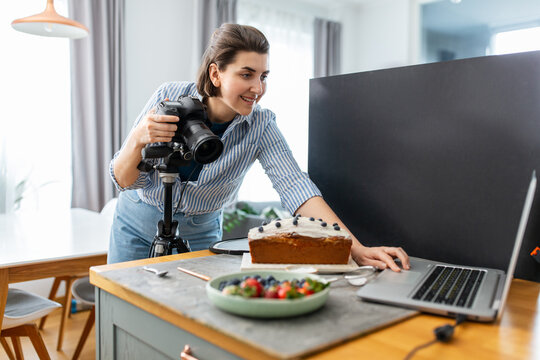 blogging, profession and people concept - happy smiling female food photographer with laptop computer and camera photographing cake in kitchen at home