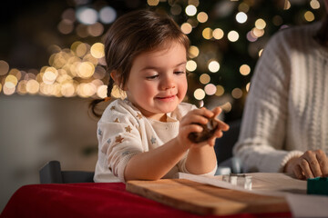 family, cooking and winter holidays concept - happy mother and baby daughter having fun with dough for gingerbread cookies at home on christmas