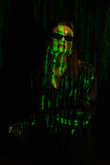 fashionable woman in sunglasses and silver accessories posing in green neon light isolated on black
