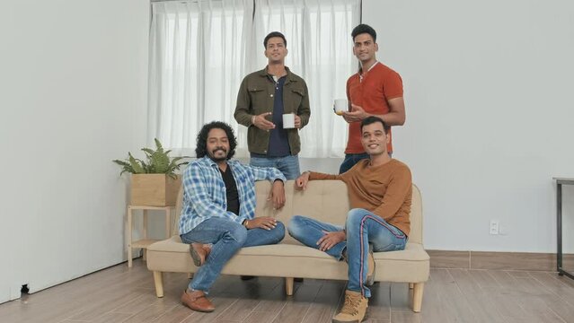 Slowmo portrait of four Indian male colleagues chatting during coffee break in office then looking at camera
