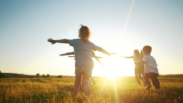 kids run in the park at sunset. friendly family children camp kid dream concept. a group of children run on the grass at the rays fun of the sun silhouette. childhood sunset dream teamwork concept