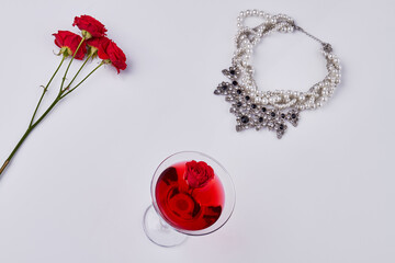 Flat lay womens accessories on white background. Red cocktail with rose flowers and necklace.