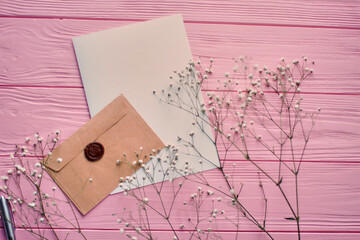 Top view envelope with blank paper and spring flowers. Pink wooden desk background.