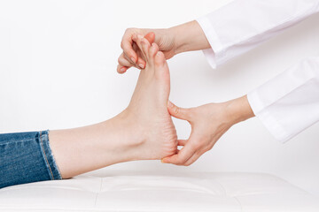 Examination of a young woman by an female orthopedist. Cropped shot of doctor in a white coat holding a painful foot in her hands. Flat feet, injury. Foot treatment. Pain from uncomfortable shoes