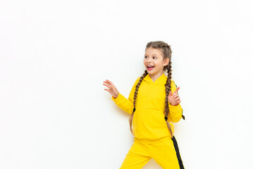 A little girl with long braids looks at your advertisement and smiles. A child in a yellow sports suit on a white isolated background. Copy space.