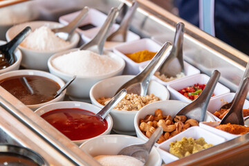 Sauces, spices and nuts for Thai cooking in white bowls, close-up angled view, with spoons