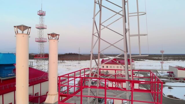 A drone flies near a metal tower for plant lighting in winter, a petrochemical plant aerial view of the plant and lightning rod towers protecting equipment. Fuel crisis in winter.