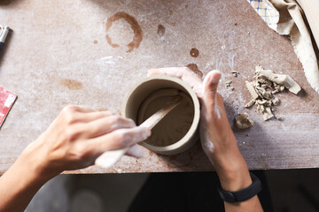 Obraz na płótnie Canvas Female ceramist working in pottery studio. Ceramist's Hands Dirty Of Clay. Process of creating pottery. Master ceramist works in her studio