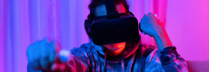 Naklejka premium Man wears virtual reality glasses and uses joystick to play games with fun, VR, Future games, Technology, Red and blue background, Touch Controller, Bluetooth Remote Controller, VR game concept.