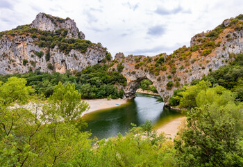 Fototapeta na wymiar “Pont d’Arc“ panorama in Vallon South France. Large natural bridge or rock arch spanning over Ardèche river in Provence. Major tourist attraction and sight in calm morning atmosphere on a cloudy day.