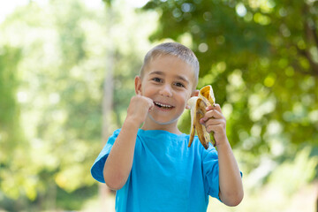 happy little boy eats banana in nature