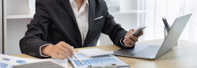 Finance workers are reviewing the company's financial data on a laptop and using smartphones to...