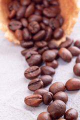 Vertical shot close up of coffee beans. Waffle ice cream cone with spilled grains.