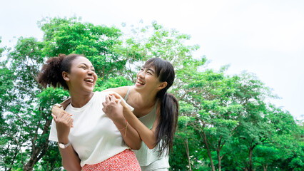 Fototapeta premium Smiling two young diversity African American Asian women friends having fun in a nature, park queer non-binary gender identity, gay lesbian love romance, boho summer vacation style.