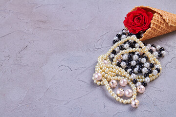 Ice cream cone with pearl necklaces and rose flower. Putty background with copy space.