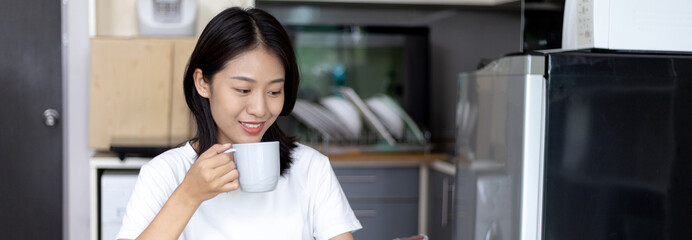 Fototapeta na wymiar Asian woman eats breakfast with crackers (Healthy whole grain) and juice, Use your phone or mobile phone to search for morning news, Small room in condominium background, Wake-up activities.