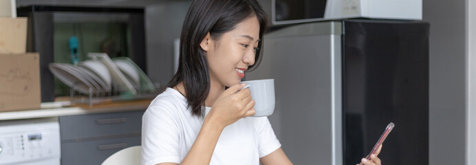 Fototapeta na wymiar Asian woman eats breakfast with crackers (Healthy whole grain) and juice, Use your phone or mobile phone to search for morning news, Small room in condominium background, Wake-up activities.