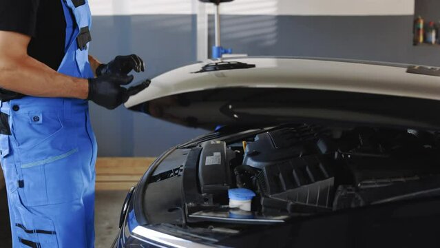Unrecognizable automotive mechanic man open a car hood and check up the engine. Vehicle service manager worker work in mechanics garage, check and maintenance to repair the motorcar car in workshop