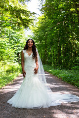 Obraz na płótnie Canvas beautiful african-american bride standing in a white gown outdoors in nature