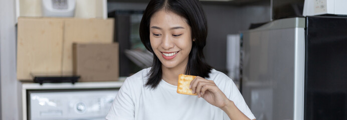 Fototapeta na wymiar Asian woman eats breakfast with crackers (Healthy whole grain) and juice, Use your phone or tablet to search for morning news, Small room in condominium background, Wake-up activities..